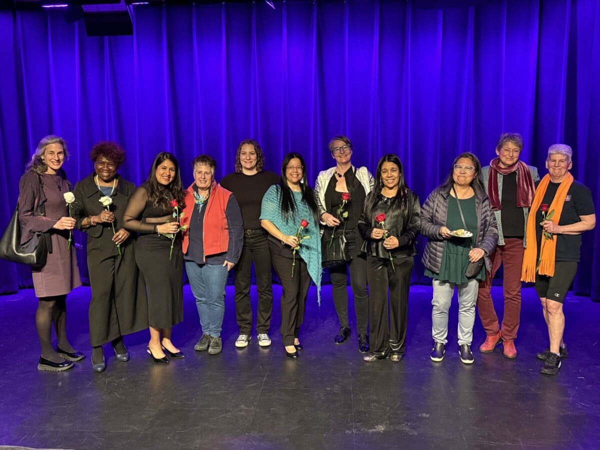 the writing sisters on stage in front of a blue velvet stage curtain all the women are holding roses and smiling